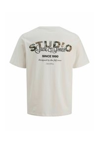 Krótki rękaw, kremowa bawełniana koszulka z nadrukiem na plecach z napisem "STUDIO" i "Jack & Jones" w stylizowanych czcionkach.