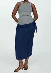 Dunkelblaue Denim-Wickelröcke mit seitlichem Bindeband und glatter Textur. Kombiniert mit einem enganliegenden grauen Tanktop und schwarzen Sandalen mit Riemchen.