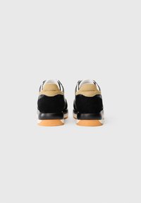 Sorte og beige sneakers med overdel i ruskinn og læder, hvit mellomsåle og oransje gummisåle, med logo på hælen.