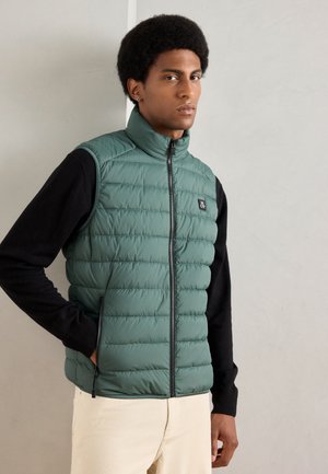 Groene gewatteerde vest met hoge kraag, ritsluiting en een logopatch. Gedragen over een zwarte longsleeve, met een soepele, gewatteerde textuur.
