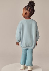 Lyseblå oversized sweatshirt med ribbede manchetter, parret med matchende tætsiddende bukser med en frynset kant. Hvide sneakers fuldender looket.