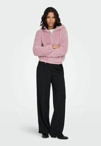 Roze, zachte zip-up hoodie met capuchon, gecombineerd met hooggetailleerde zwarte wijde broekspijpen. Gladde stoftextuur met zijzakken.