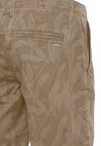 Pantalones cortos color caqui con un patrón texturizado de hojas y un bolsillo trasero. Presenta un pequeño logotipo en la parte posterior. Fabricado con un tejido ligero.