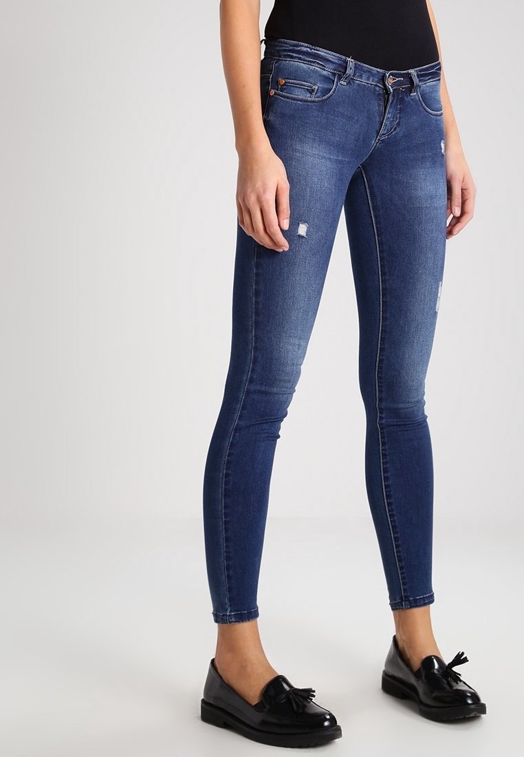 Jeans ajustados en denim azul oscuro con detalles desgastados. Cuentan con un diseño clásico de cinco bolsillos y cierre de botón metálico.