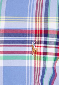 Tessuto scozzese blu e bianco con strisce rosse, verdi e gialle. Dettaglio notevole: logo ricamato di un cavallo vicino al centro.