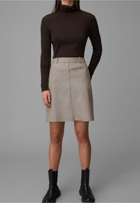 Ruskopäinen ribbed turtleneck -paita, johon on yhdistetty beige ruudullinen hame, jossa on suora muoto ja sileä kangaspinta, käytetty mustien nilkkureiden kanssa.