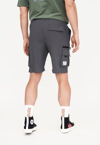 Grå cargoshorts med flera fickor, elastisk midja och avslappnad passform. Svarta högskor och vita strumpor med orange text är påbäddade.