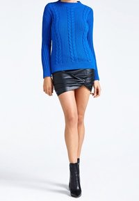 Sininen neulottu pusero kierrekuviolla, pitkät hihat, yhdistetty mustaan nahkaiseen minihameeseen, jossa on kiertyvä muotoilu. Mustat nilkkurit.