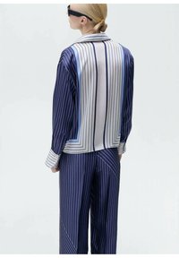 Námořnický a světle modrý pruhovaný saténový outfit obsahující košili s dlouhým rukávem a límcem a volně střižené kalhoty s geometrickými akcenty.