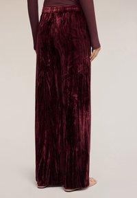 Burgundowe welurowe spodnie z szerokimi nogawkami o gładkiej teksturze i wysokim stanem, z subtelnymi pionowymi liniami i swobodną sylwetką.