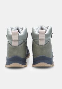 Botas de senderismo verdes con un collar acolchado, forro de piel sintética y bucles de tirón beige. Suela de goma texturizada con un patrón de dibujo visible.