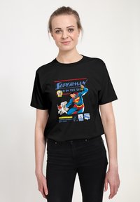 Černé tričko s potiskem zobrazujícím Supermana a jeho psa Krypto v jasných barvách, s textem "SUPERMAN NA OBTÍŽI. "