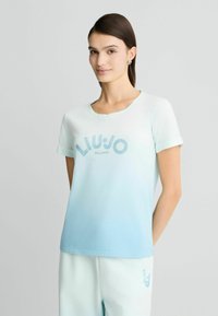 T-shirt bleu clair à manches courtes avec un col arrondi, arborant une impression "LIU JO MILANO" avec des accents bleus scintillants et un effet ombré.