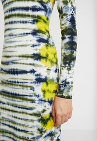 Robe à manches longues, ajustée, en tissu extensible, présentant un motif tie-dye en bleu marine, vert et jaune avec des sections blanches.