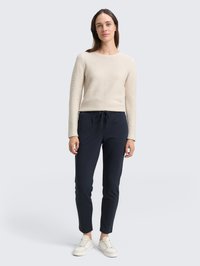 Top de manga larga beige de canalé combinado con pantalones estilo jogger azul marino, con cintura con cordón. El calzado son zapatillas blancas.