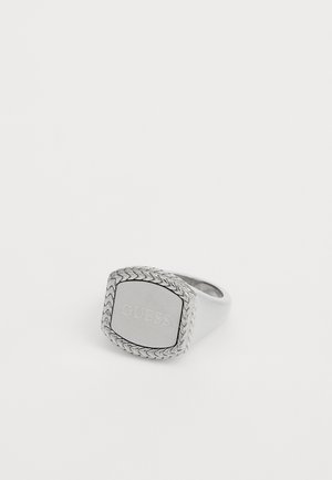 Bague en argent avec un motif rectangulaire, des détails tressés autour du bord, et gravée "GUESS" sur une surface lisse. Fini en métal poli.