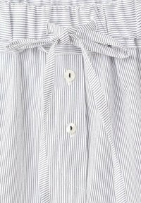 Tissu blanc avec fines rayures noires verticales, présentant un nœud noué en haut et deux boutons blancs en dessous du nœud.