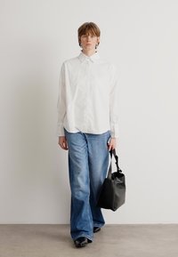 Hvit skjorte med lange ermer, lyseblå vide jeans, og en svart skinnveske. Glatte stoffer og minimalistisk design.