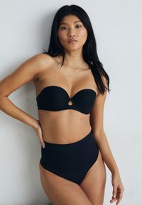 Čierny bikiny top bez ramienok s vystuženými pohárikmi a detaily v tvare kľúčovej dierky, doplnený vysokými čiernymi bikiny nohavičkami. Hladká textúra.
