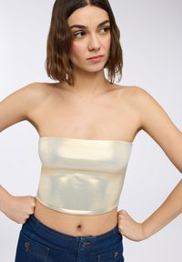 Metaliczny złoty top bez ramiączek o dopasowanym kroju, gładkiej fakturze i krótkiej długości, połączony z niebieskimi spodniami dżinsowymi z wysokim stanem.