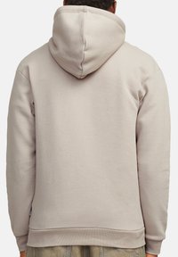 Hoodie beige avec une capuche spacieuse, des poignets et un ourlet côtelés, et un tissu doux et texturé, mettant en avant un design simple et fonctionnel.