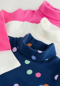 Tre polotröjor staplade: en rosa fleece, en vit slät tyg, och en blå fleece med flerfärgade prickar.