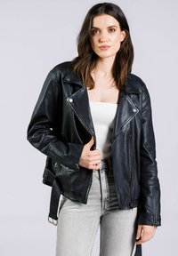 Černá kožená moto bunda s šikmým zipem a límcem na patentky. Obsahuje kapsy na zip a nastavitelné popruhy v pase. Nošeno s šedými džíny.