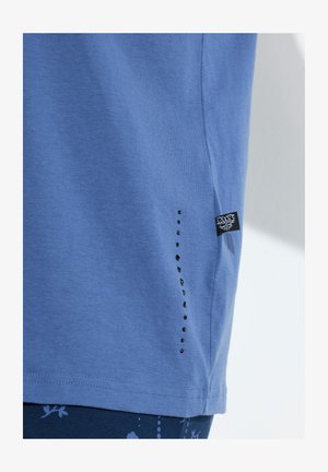 Hellblaues Baumwoll-T-Shirt mit rundem Ausschnitt, kurzen Ärmeln und einer vertikalen Reihe schwarzer dekorativer Nieten an der Seite.