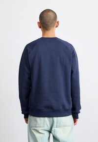 Mørkeblå sweatshirt med rund hals, raglanærmer og ribbede manchetter. Glat tekstur, minimalistisk design og ingen synlige logoer eller mønstre.
