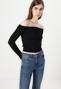 Black off-the-shoulder ribbed crop sweater with long sleeves, paired with blue high-waisted jeans, featuring a classic five-pocket design.