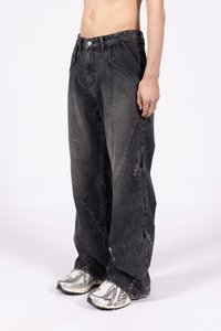 Czarne dżinsowe spodnie o szerokiej nogawce charakteryzują się wysokim stanem, charakterystycznymi kątowymi szwami i zapięciami na zatrzaski na nogawkach. W zestawieniu z szarymi butami sportowymi.