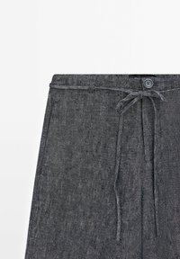 Dark gray trousers with a textured fabric, featuring a drawstring tie at the waist and a button closure. Simple design with minimal detailing.