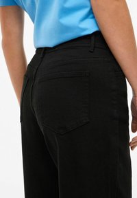 Czarne jeansy z denimu z dopasowaną talią, dwoma tylnymi kieszeniami i przeszyciami w tonacji. Dopasowane do jasnoniebieskiej koszulki o luźnym kroju.