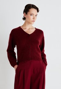 Burgundy button-up cardigan with a V-neck, long sleeves, and a soft texture. Paired with matching high-waisted trousers.