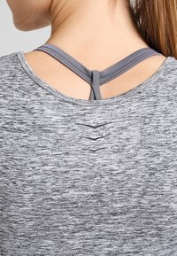 Grauer Sporttop aus strukturiertem Stoff mit einem Melange-Muster, Racerback-Design und dekorativen Stickdetails am Rücken.