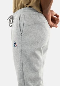 Light grey sweatpants made of soft material, featuring a drawstring waist, side pockets, and a small colored logo accent on the thigh.