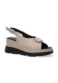 Beige slingback sandalen met een chunky zwarte zool, open teen, circulair metalen accent en leren bovenwerk voor ondersteuning en comfort.