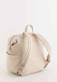 Mochila texturizada beige con un compartimento principal con cremallera, dos correas para los hombros y un bolsillo lateral. Cuenta con acentos de herrajes en tono dorado.