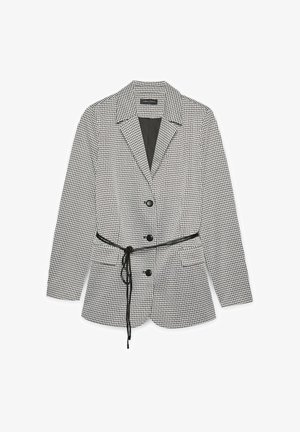 Zwart-witte houndstooth blazer met reverskraag, drie zwarte knopen, twee voorke pockets en een dunne zwarte riem geknoopt in de taille.