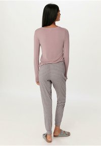 Long-sleeve, mauve top with a relaxed fit, paired with gray-striped lounge pants and gray slip-on slippers, viewed from the back.