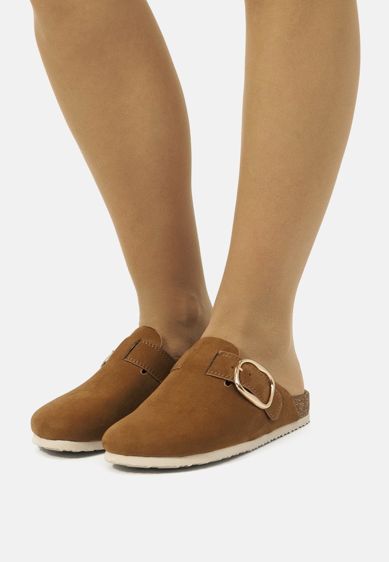 Chaussures slip-on en cuir suédé marron à bout rond, dotées d'une grande boucle métallique et d'un accent en liège texturé sur le côté.