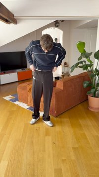 Svarte plisserte bukser med høyt liv og elastisk midjebånd, kombinert med en marineblå glidelåsjakke og sølvfargede joggesko.