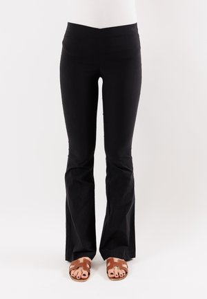 Pantaloni neri a palazzo realizzati in tessuto elasticizzato con una texture liscia. Vita alta e abbinati a sandali marroni.