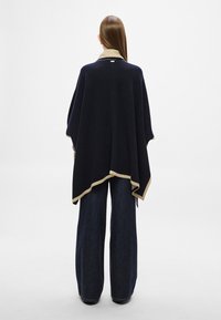 Ναυτικό πόνετσο με ταμπά τελείωμα, μαλακή υφή και ασύμμετρο τελείωμα· φορεμένο πάνω από φαρδιά σκούρα τζιν παντελόνια.