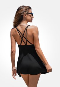 Zwart zwempak met een uitlopend rokje, kruisende bandjes op de rug en een gladde textuur, ideaal voor strandkleding.
