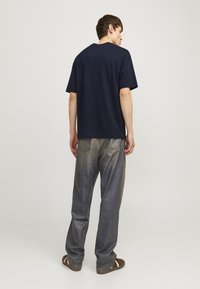 Marineblå kortærmet T-shirt, afslappet pasform, lavet af bomuldsstoff, parret med løstsiddende mørkeblå denimjeans og brune sandaler.