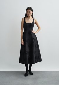 Μαύρο αμάνικο φόρεμα με εφαρμοστό μπούστο και φουσκωτή φούστα. Διαθέτει κεντήματα με λουλουδάτα χάντρες και ύφασμα με ομαλή υφή.