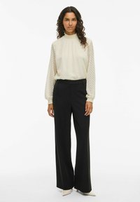 Cream blouse with a textured chevron pattern and high neck, paired with black wide-leg trousers and pointed beige heels.