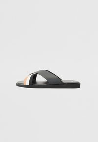 Svarta slidesandaler med korsade remmar, med en beigefärgad och vit accentrand vid tån. Tillverkade av slät syntetisk material.