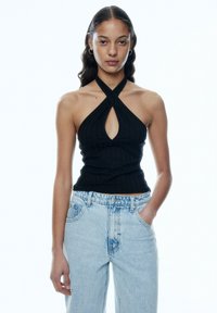 Zwarte geribbelde haltertop met een sleutelgat uithulling, gecombineerd met lichtblauwe high-waisted jeans met een relaxte pasvorm en klassieke zakken.